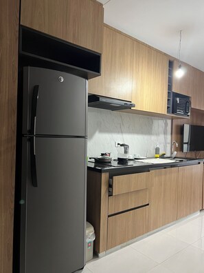 A modern kitchen with a stainless steel refrigerator, wooden cabinets, a microwave, and a black countertop. - Cozy 1-bedroom studio in enchanting Santa Cruz de la Sierra with AC (Santa Cruz de la Sierra)