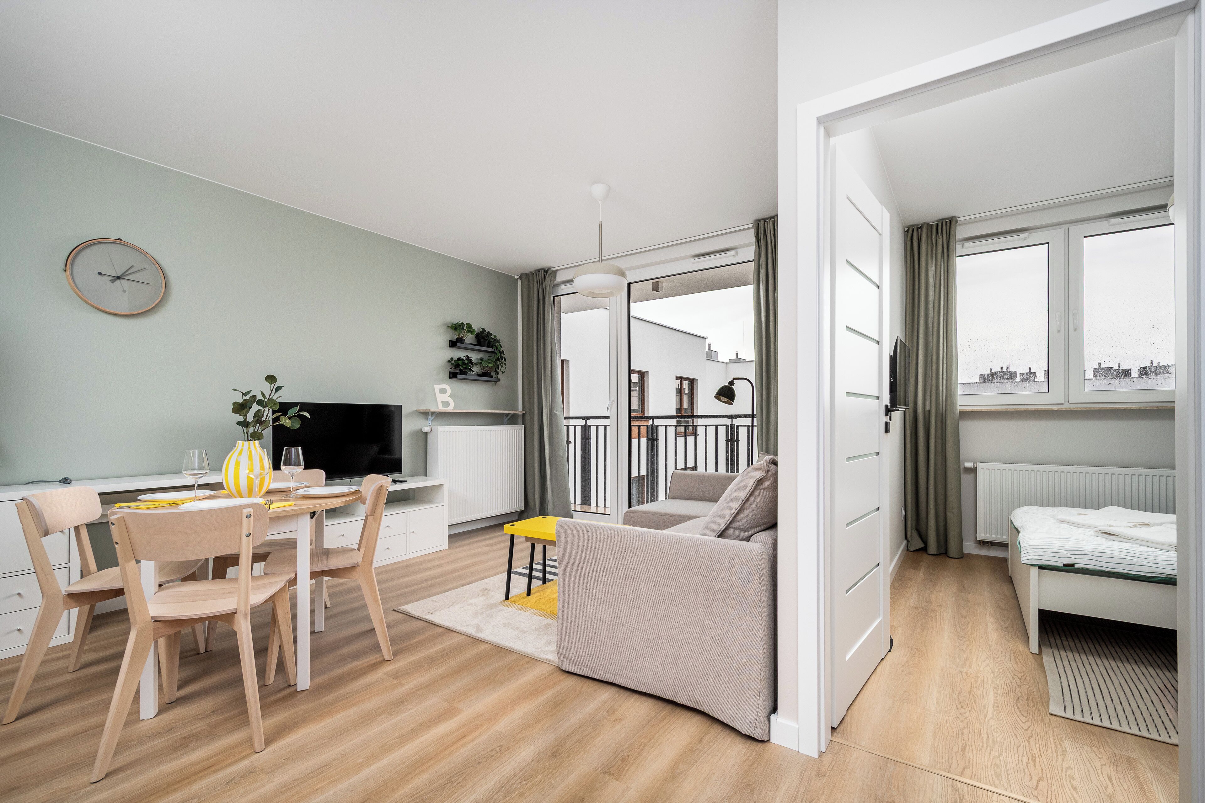 A modern living room with a dining area, a sofa, a TV, and a view of the outside.