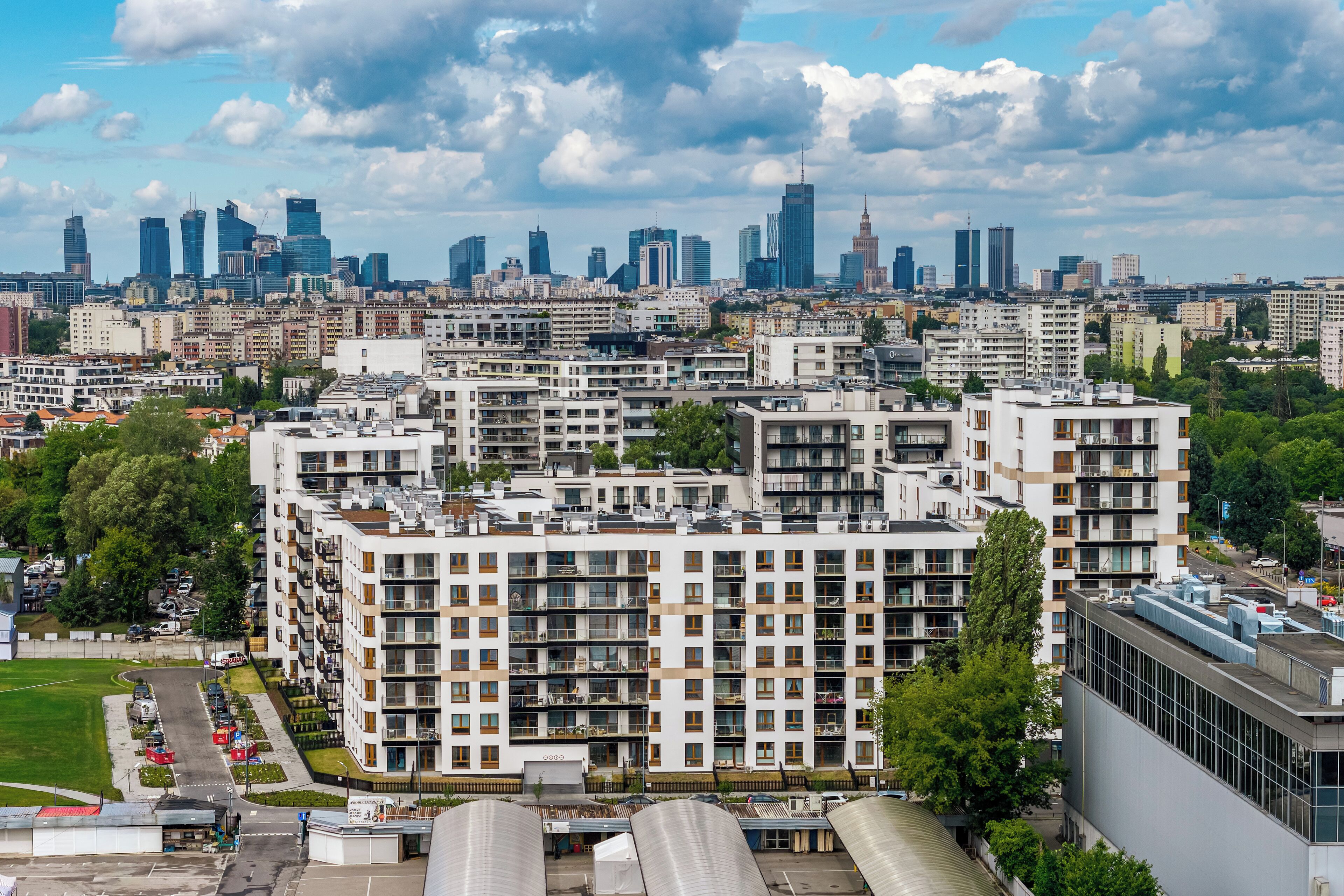 Un immeuble résidentiel de grande hauteur, doté de nombreux balcons, entouré d’autres bâtiments et avec une vue sur les toits de la ville en arrière-plan.