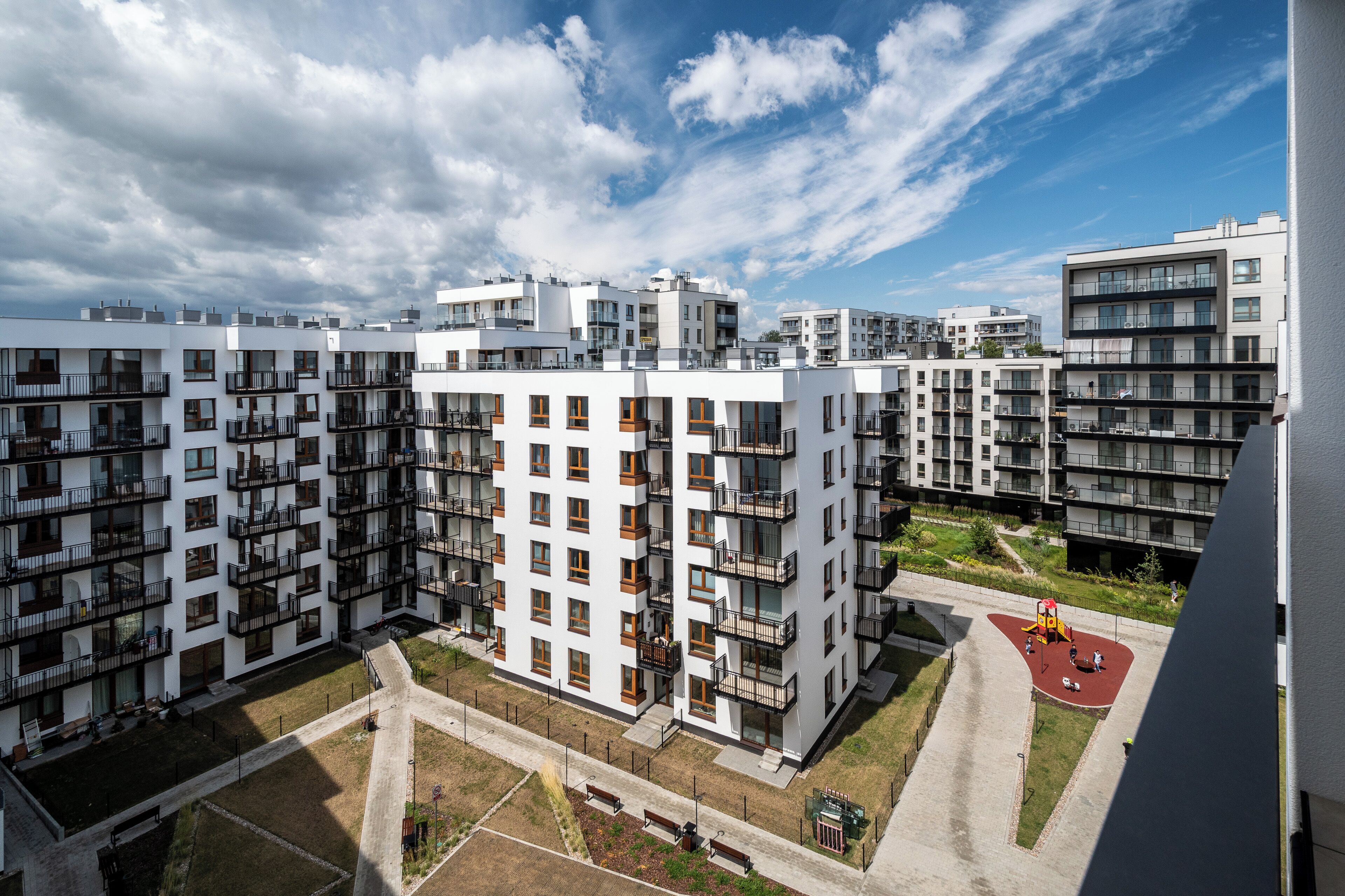 A modern apartment complex with multiple buildings, balconies, and a playground area.