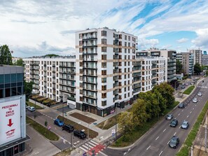 Un edificio residencial de varios pisos con balcones, una acera y una calle con automóviles.