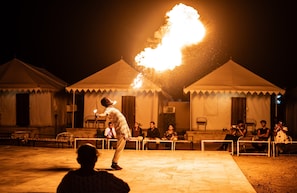 Una persona realizando un espectáculo de fuego frente a carpas, de noche.