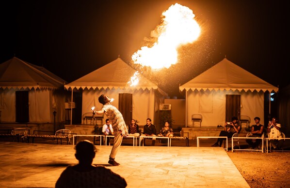 A person performing a fire act in front of tents at night.