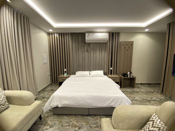 A hotel room with a large bed, two bedside tables, a wardrobe, and a ceiling-mounted air conditioning unit.