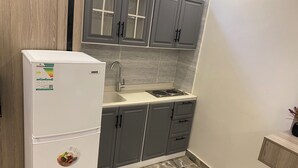 A compact kitchen with grey cabinets, a white refrigerator, a sink, and a stove. - Studio Apartment in Al Hamdaniyah- J14 (Jeddah)