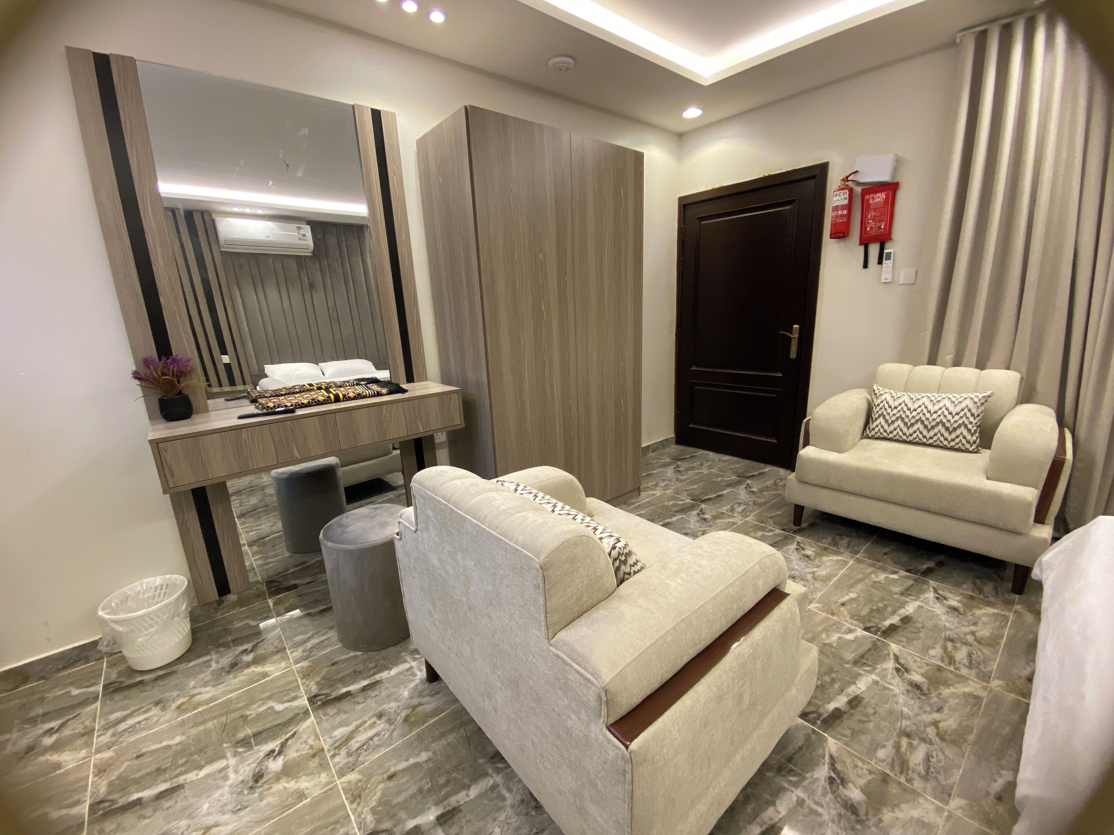 A modern hotel room with a bed, a sofa, a desk with a mirror, and a door.