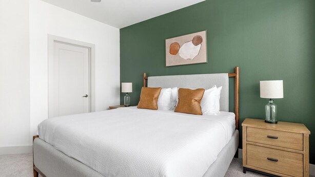 Une chambre à coucher bien rangée, avec un lit, des tables de chevet et une œuvre d’art accrochée au mur.