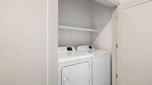 Une buanderie avec deux machines à laver à chargement frontal blanches et une étagère blanche au-dessus.