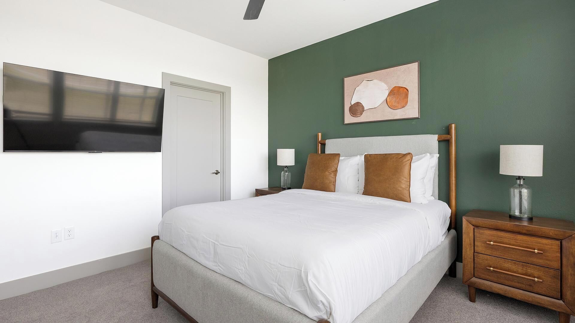 Une chambre à coucher avec un lit, des tables de chevet, un téléviseur fixé au mur et un tableau.