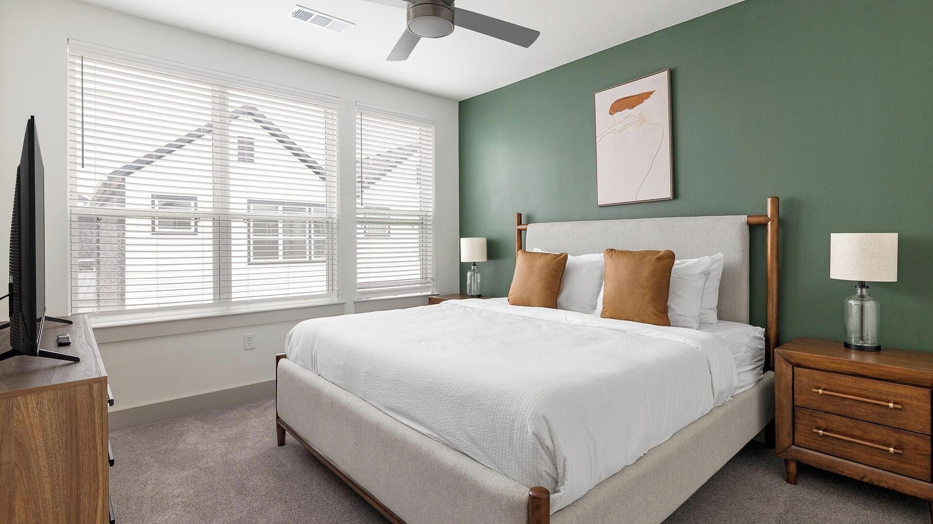 A bedroom with a bed, nightstands, a lamp, a ceiling fan, and a window with blinds.