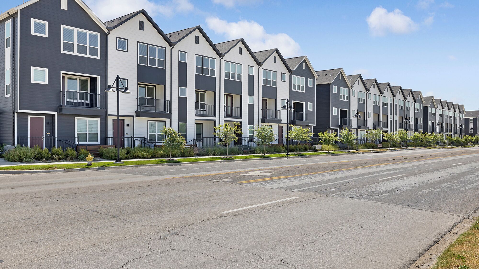 A row of modern townhouses with balconies, a clear sky, and a well-maintained street.