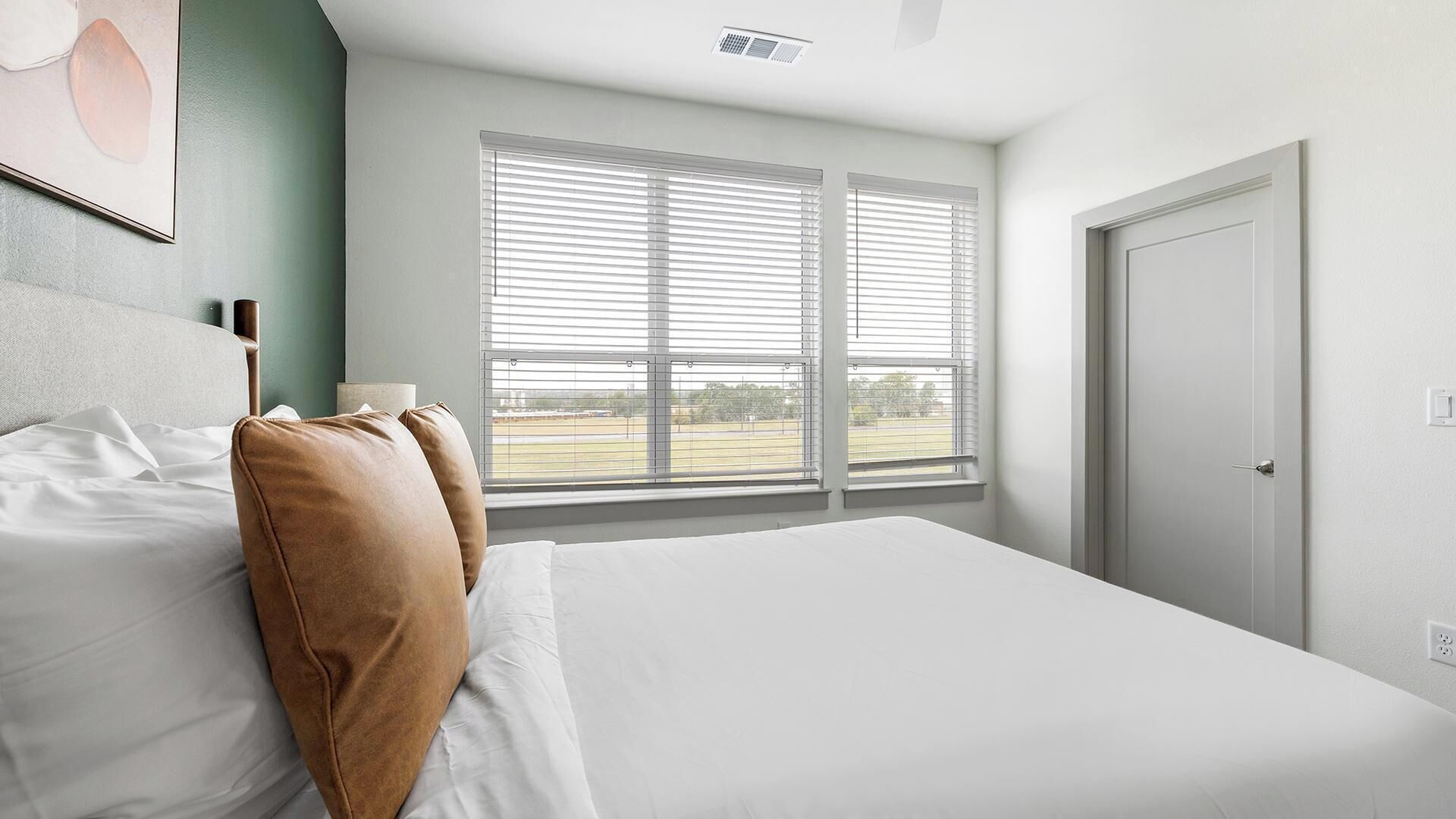 A bedroom with a bed, two pillows, a window with blinds, and a door.