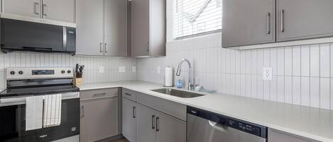 A modern kitchen with grey cabinets, stainless steel appliances, and a window with blinds.