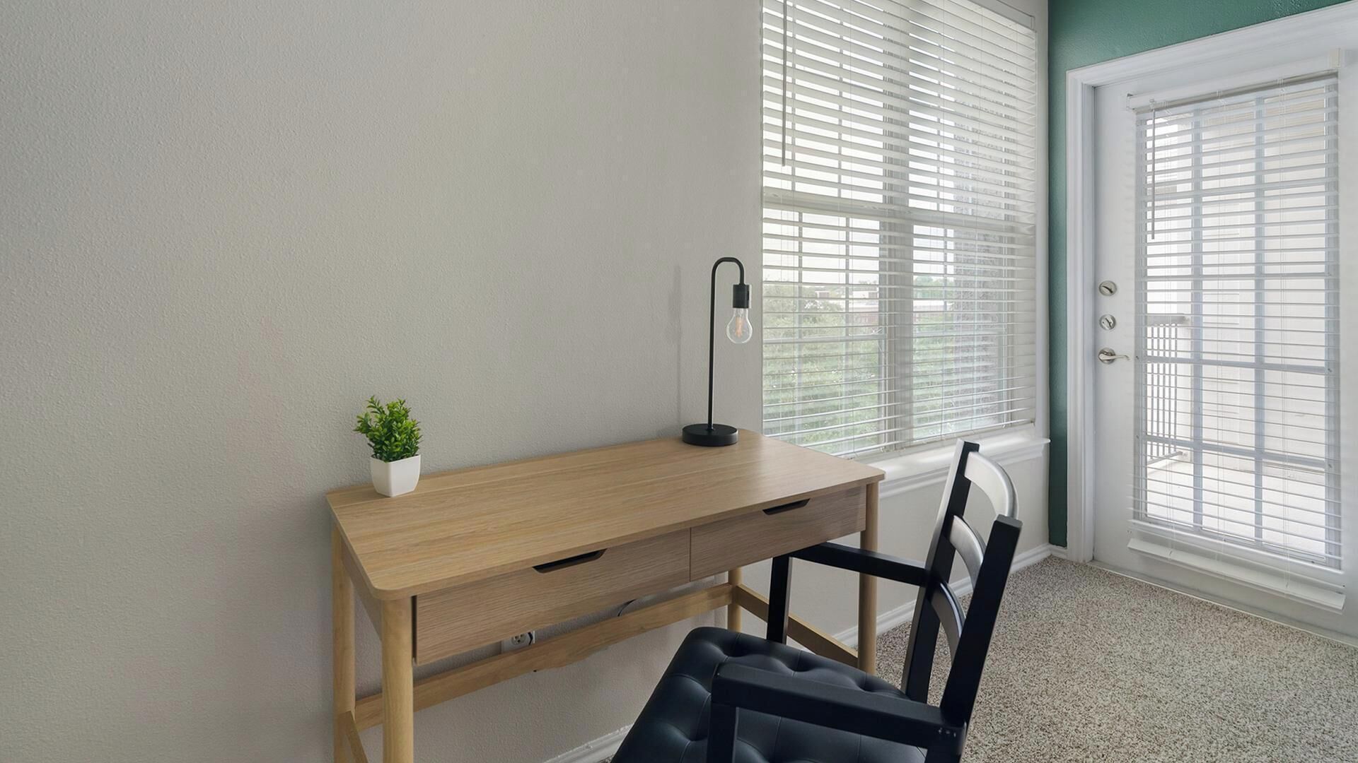 A room with a wooden desk, a chair, a potted plant, and a floor lamp.
