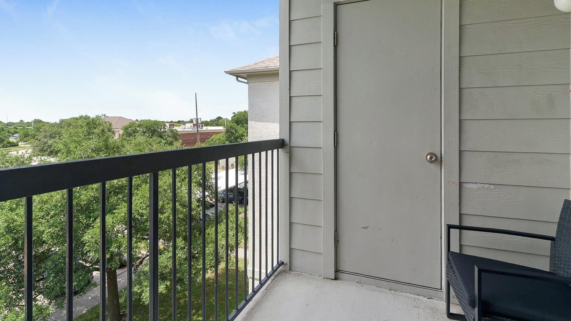 A balcony with a metal railing, a door, and a view of a residential area with trees and houses.