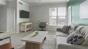 A living room with a sofa, coffee table, TV, and a desk with a chair. - Landing Amazing 1BD in Copperfield (Houston)