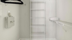 Ein weißes Zimmer mit einer weißen Metallregaleinheit an der Wand, einem weißen Handtuchhalter und einem weißen Elektroverteiler.