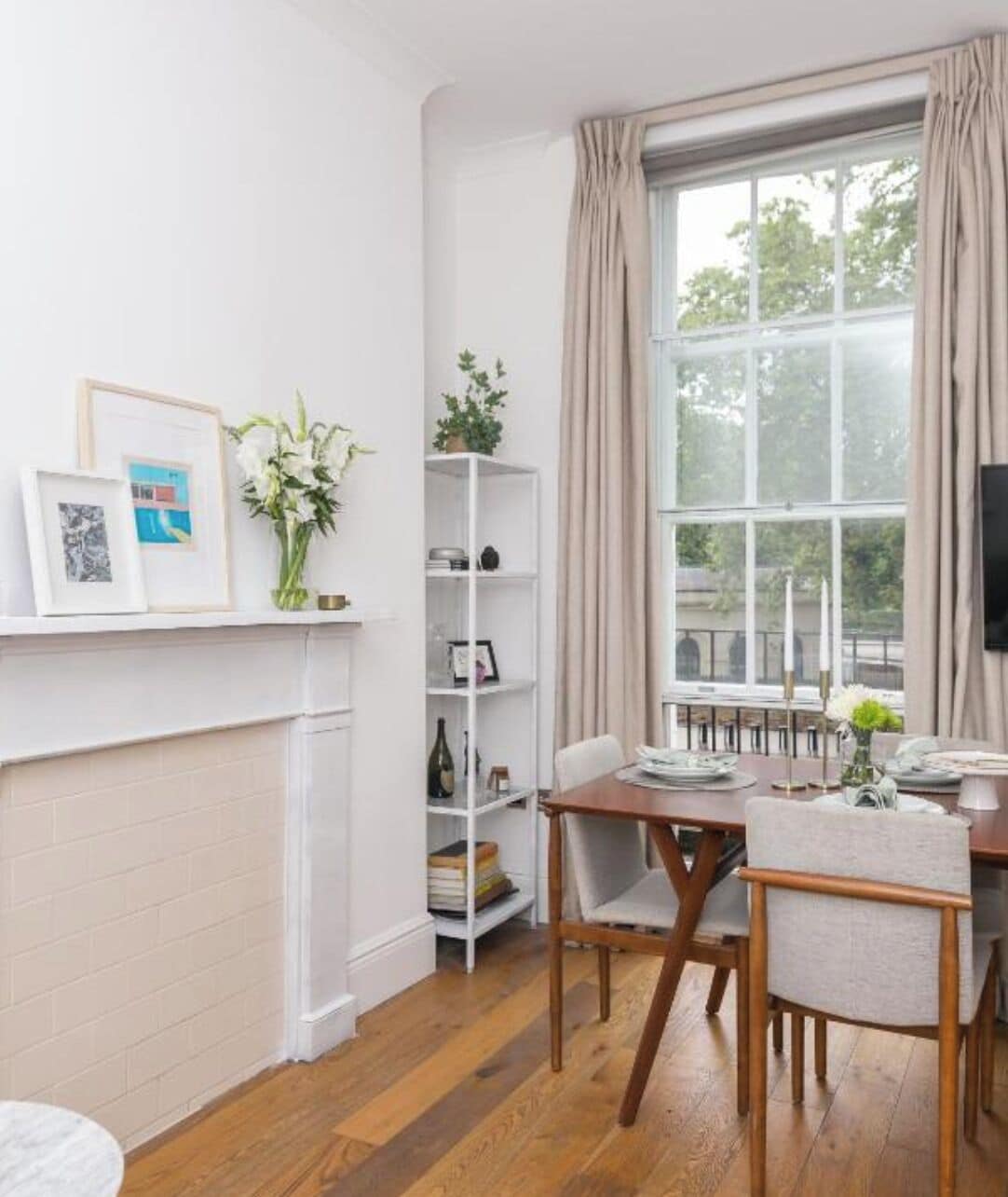 A dining area with a table, chairs, a bookshelf, and a window with curtains.