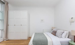 Ein Schlafzimmer mit Bett, Nachttisch, Lampe, Kleiderschrank und einem Fenster mit Vorhängen.