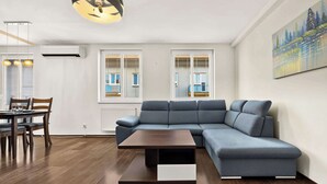 Ein modernes Wohnzimmer mit einer Eckcouch, einem Esstisch mit Stühlen und einem Bild an der Wand.