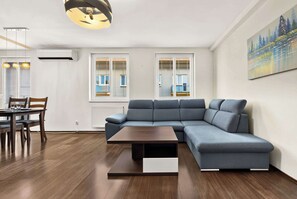 A modern living room with a sectional sofa, a dining table with chairs, and a painting on the wall. - Homely Apartment with Balcony - Central BA (Bratislava)