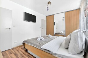 A modern bedroom with a bed, a flat-screen TV, a wardrobe, and a mirror. - Homely Apartment with Balcony - Central BA (Bratislava)