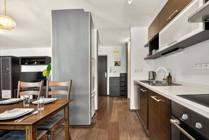 A modern kitchen with a dining area, featuring a built-in oven, a sink, and a refrigerator. - Homely Apartment with Balcony - Central BA (Bratislava)