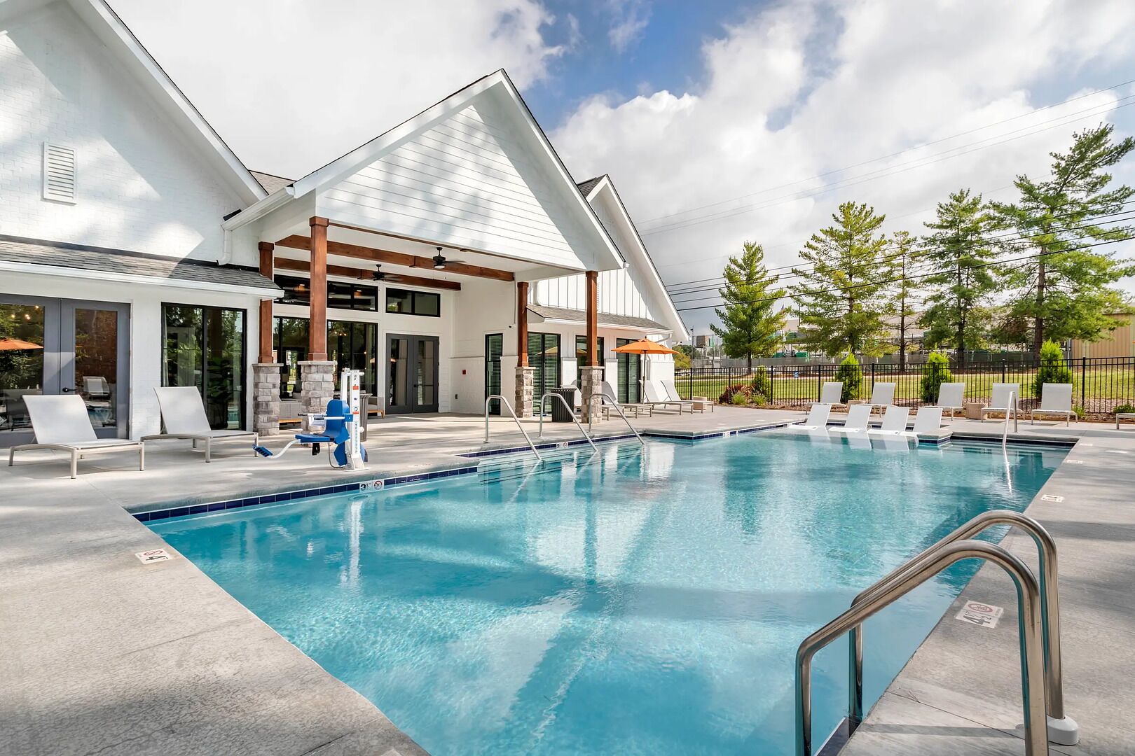 A swimming pool with lounge chairs and a covered area, surrounded by a building with large windows and a stone pillar.