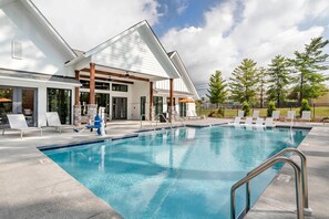 A swimming pool with lounge chairs and a covered area, surrounded by a building with large windows and a stone pillar. - Landing Amazing 1bd, Gym (Knoxville)