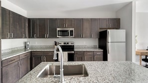 A modern kitchen with dark cabinets, a stainless steel sink, granite countertops, a microwave, an oven, and a refrigerator. - Landing Amazing 1bd, Gym (Knoxville)