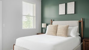 A bedroom with a bed, two wall-mounted picture frames, a nightstand with a lamp, and a window with blinds. - Landing Amazing 1bd, Gym (Knoxville)