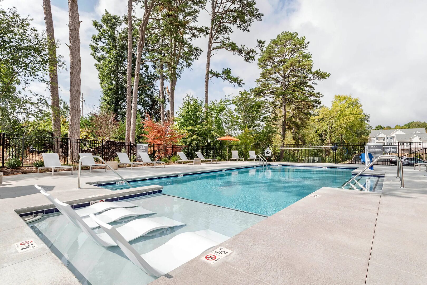 A swimming pool with lounge chairs, a lifeguard on duty sign, and a fenced area.