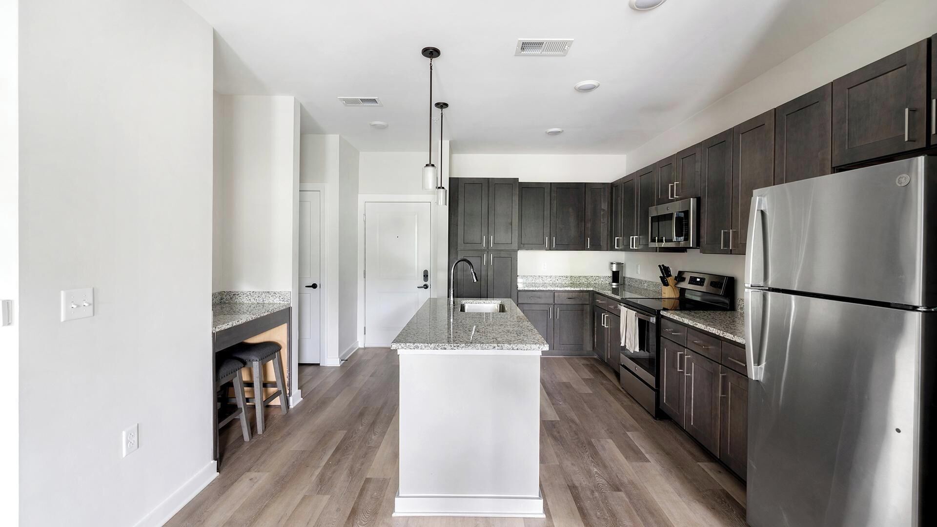 A modern kitchen with dark cabinets, stainless steel appliances, and a granite countertop.