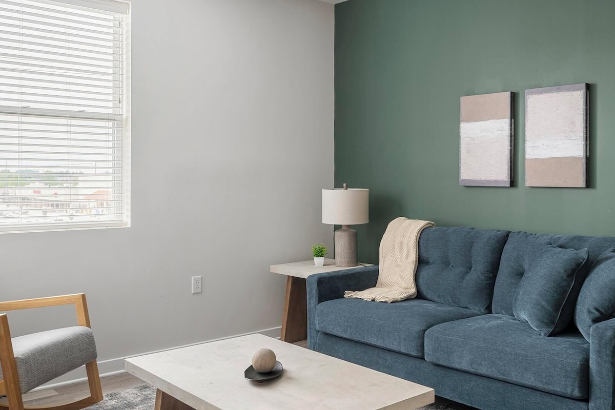 A living room with a blue sofa, a small table, a lamp, and two artworks on the wall.