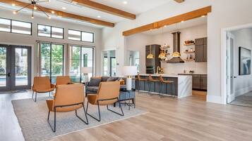 A spacious living area with a dining set, a kitchen with modern appliances, and large windows providing natural light.