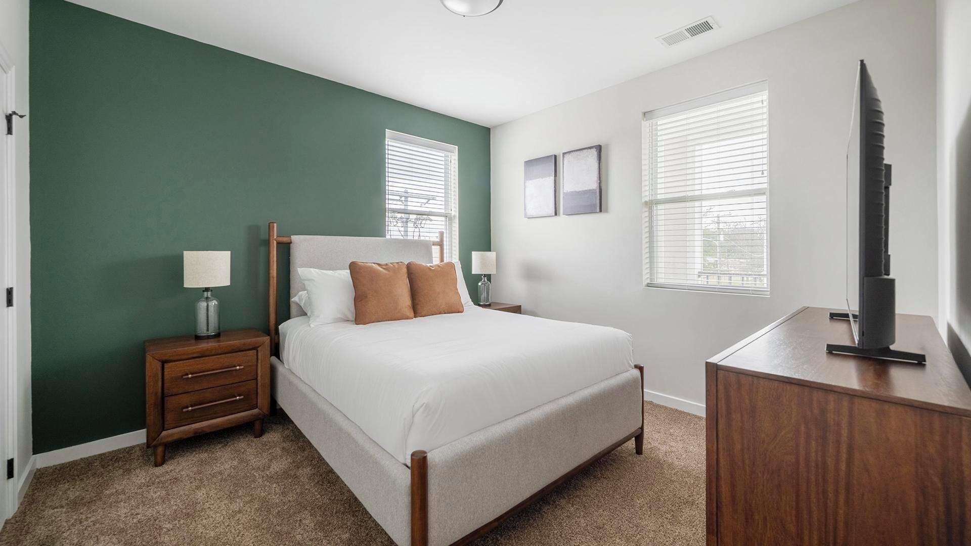 A bedroom with a bed, bedside tables, a dresser, and a TV.