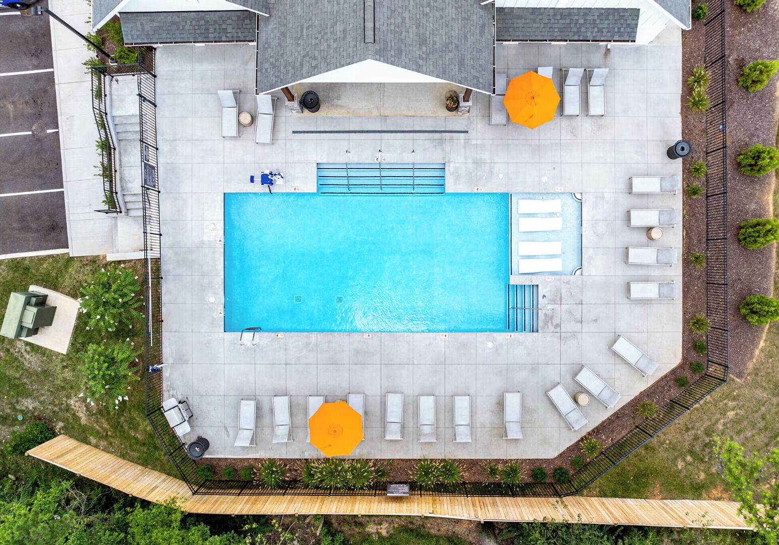 An aerial view of a rooftop pool area with a rectangular pool, multiple lounge chairs, and two umbrellas.