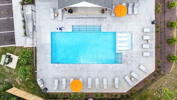 An aerial view of a rooftop pool area with a rectangular pool, multiple lounge chairs, and two umbrellas.