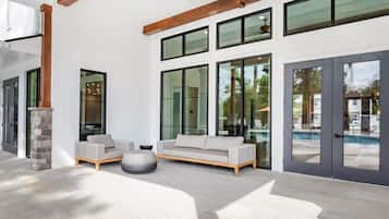A modern outdoor seating area with a sofa and chairs, a stone pillar, and a view of a swimming pool through large glass doors.