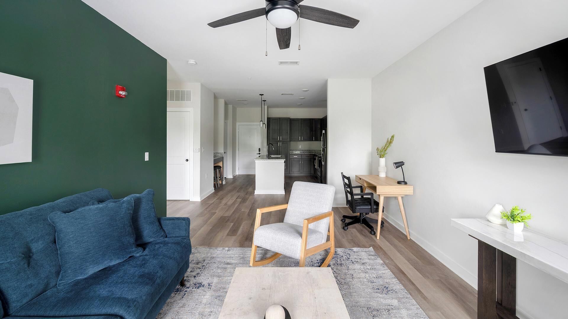 A modern living room with a sofa, a chair, a coffee table, a TV, and a kitchen in the background.