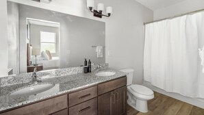 Een badkamer met een granieten aanrecht, twee wasbakken, een toilet en een douchegordijn.