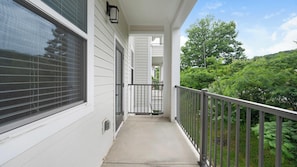A covered balcony with a metal railing, a window with blinds, and a view of a green landscape. - Landing Amazing 1bd, Gym (Knoxville)