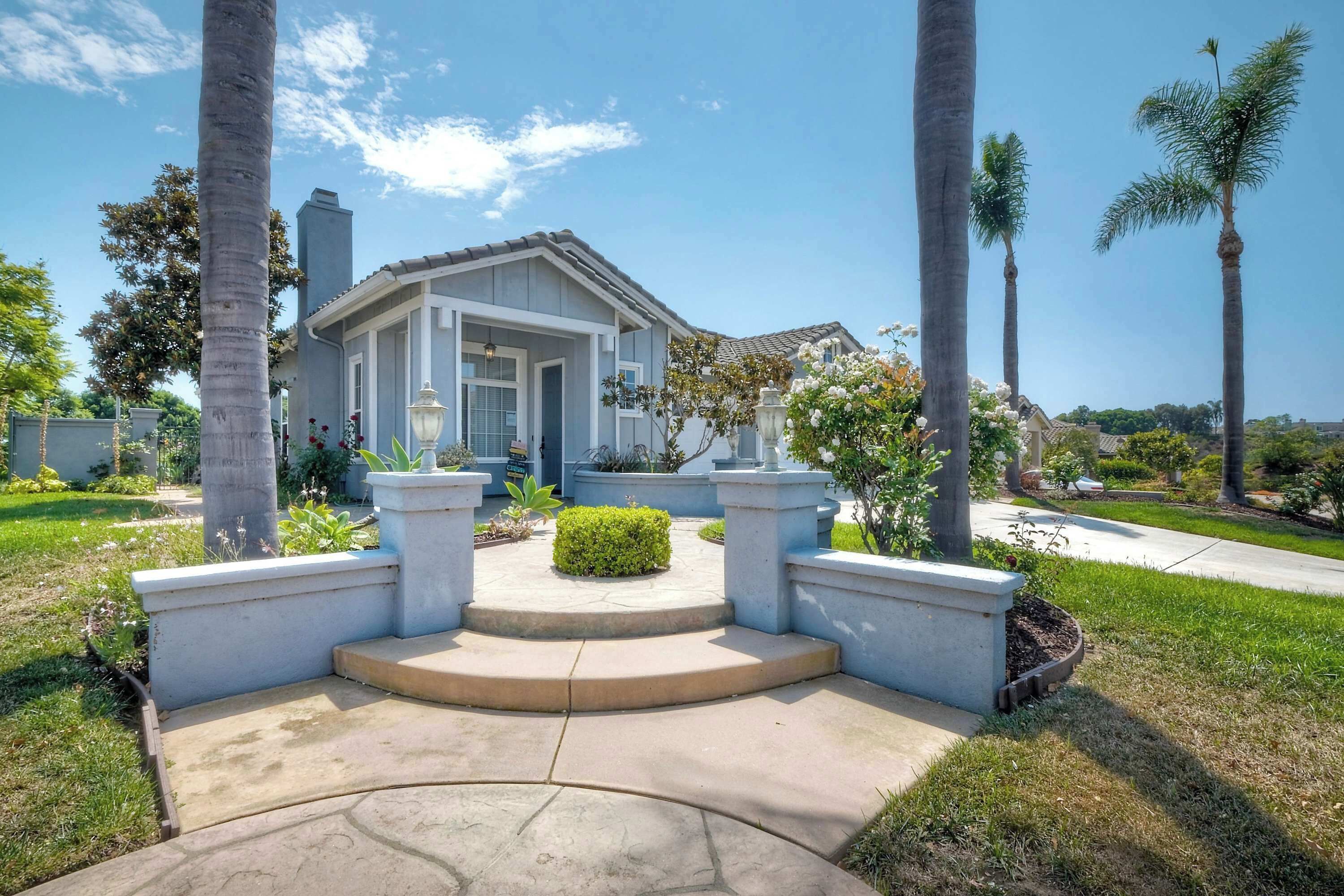 A residential property with a front entrance, a driveway, and a well-maintained garden with palm trees and shrubs.