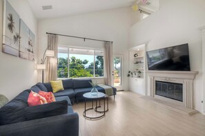 Ein geräumiges Wohnzimmer mit einem großen Fernseher, einem Kamin und einem Balkon mit Vorhängen.