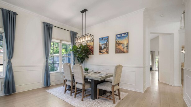Comedor con mesa de madera, cuatro sillas, lámpara colgante y dos carteles en la pared.