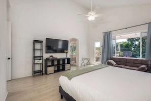 A bedroom with a bed, a TV, a console table, a sofa, and a window with curtains. - Brick & Beach Family Retreat (Carlsbad)
