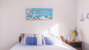 A bedroom with a bed, pillows, a nightstand, a framed picture, and a wall decoration. - Apartamento no Guaruja com Vista para o Mar (Guarujá)