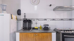 A kitchen with a refrigerator, a coffee machine, a kettle, and a stove. - Apartamento no Guaruja com Vista para o Mar (Guarujá)