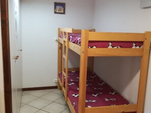 Ein Zimmer mit Etagenbett, einer Tür, einer Wand mit einem gerahmten Bild und einem gefliesten Boden.
