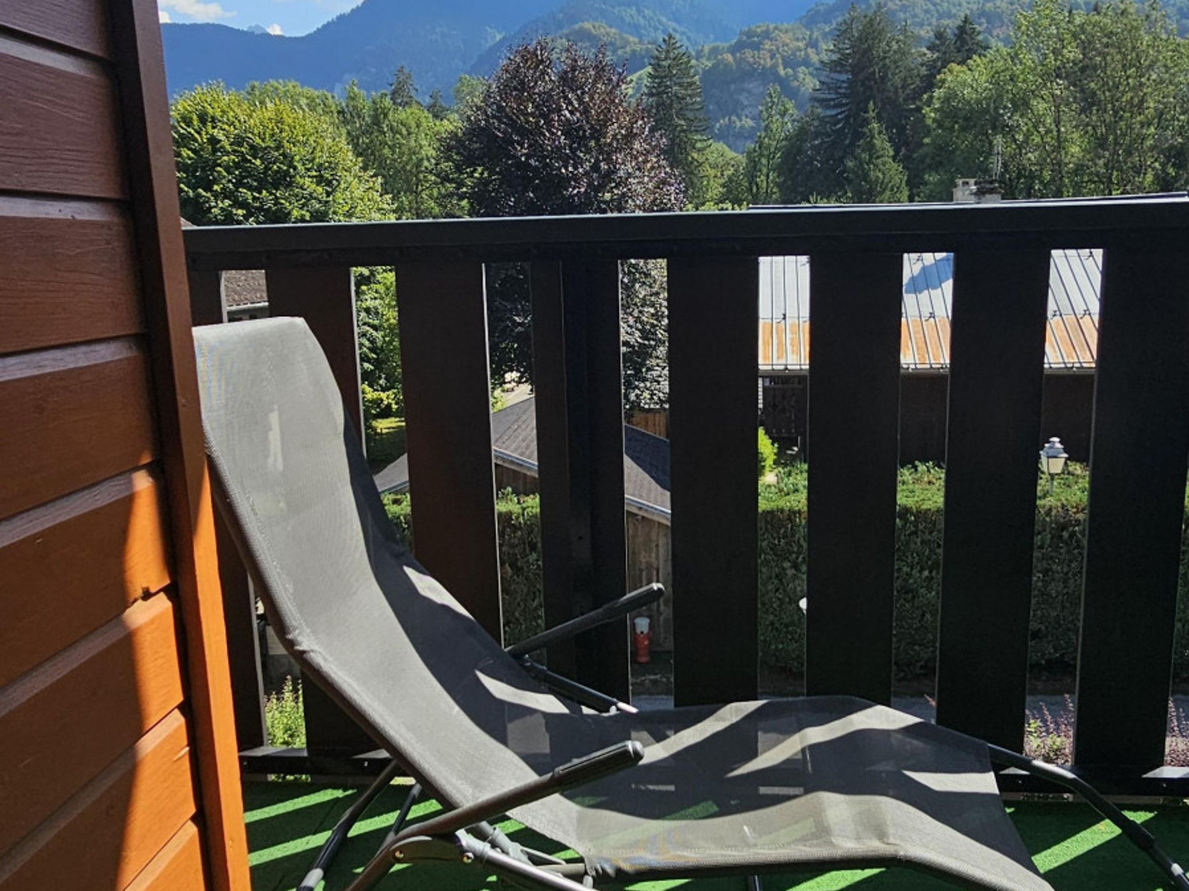 Een balkon met een metalen hekwerk, een enkele loungestoel en uitzicht op een berglandschap en bomen.